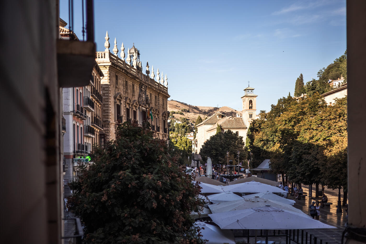 Plaza Nueva desde un balcón del apartamento Hermosa 7: las sombrillas blancas de las terrazas, a la izquierda la fachada con pináculos de la Real Chancillería y, al fondo, la torre de ladrillo de la iglesia de Santa Ana con el cerro pelado detrás.